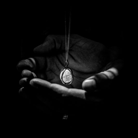 greyscape photography of pendant necklace on human hand